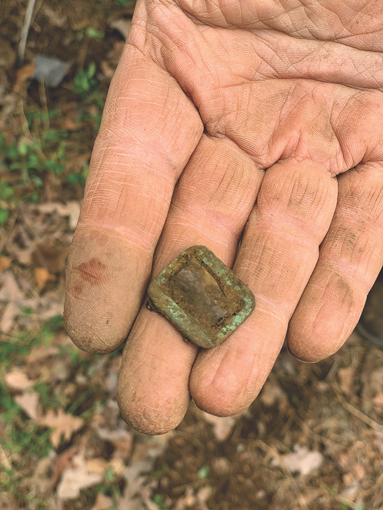 An archaeologist shows off a brass buckle from a forage cap chin strap he had recently unearthed. A portion of the leather chin strap remains in the buckle. (Photo by Melissa A. Winn) 