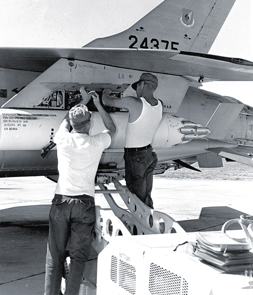 Armorers attach an SUU-7/A dispenser of CBU-2 cluster bombs on the outer wing pylon of an F-105D in 1965.