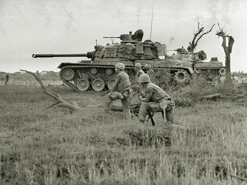 A tank offers support to a group of U.S. Marines awaiting signal to advance on trapped North Vietnamese unit near Da Ha near the DMZ, June 24, 1968. (AP Photo/Dana Stone)
