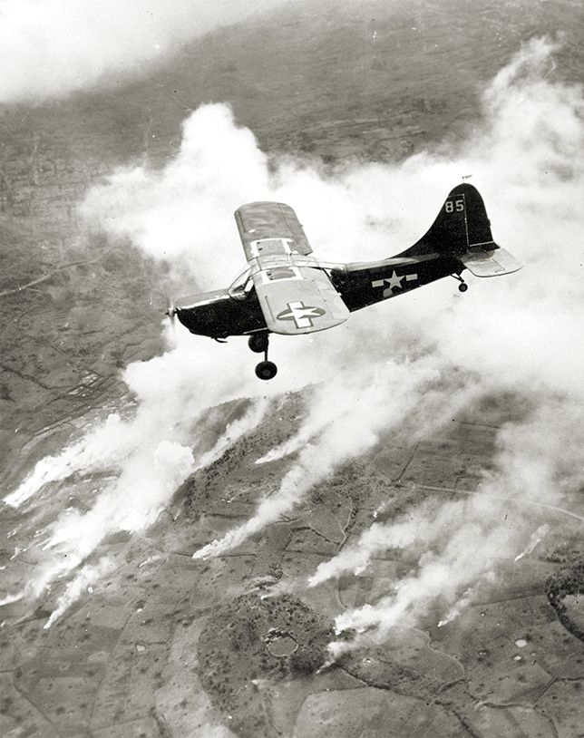 Photo of a U.S. Marine spotter plane flies an artillery control mission over the front lines on Okinawa, Japan on June 2, 1945 during World War II. Below, smoke rises from artillery and mortar fire on enemy strongpoints.