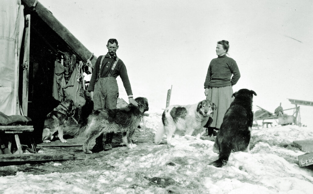 Joe and Fannie Quigley outside cabin with dogs