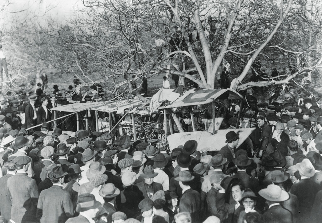 Photo of a crowd gathered around the wreckage of Lincoln Beachey's crashed aeroplane, at Ascot Park, Los Angeles, California.