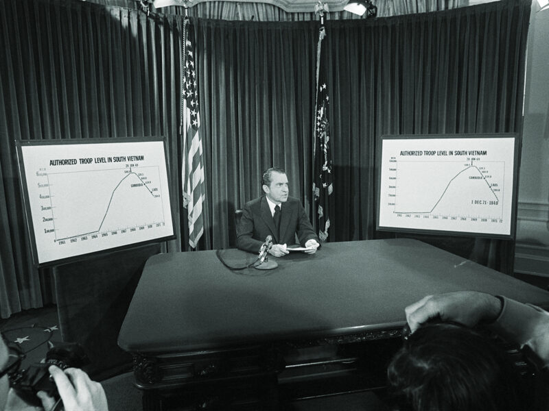Photo of President Nixon flanked by charts he used to illustrate his televised speech from the White House 4/7 in which he announced he will withdraw an additional 100,000 U.S. troops by December 1. The charts show the authorized troops level in South Vietnam.