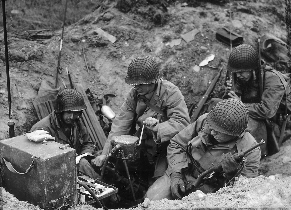 Members of a shore fire control party set up their equipment in a shell hole and start directing naval gunfire against enemy targets on June 10. The Allied fleets, totaling some 5,000 ships, had played a crucial role in supporting the landings, and continued to be needed as German resistance stiffened and the threat of a counterattack grew. Ultimately the Allies drove beyond the beachhead and past the warships’ range—only to find their progress impeded by the Norman hedgerows and German soldiers and paratroopers taking advantage of them to contest each farmer’s field down the Cotentin Peninsula that stretches from Cherbourg to Carentan and Lessay. (National Archives)